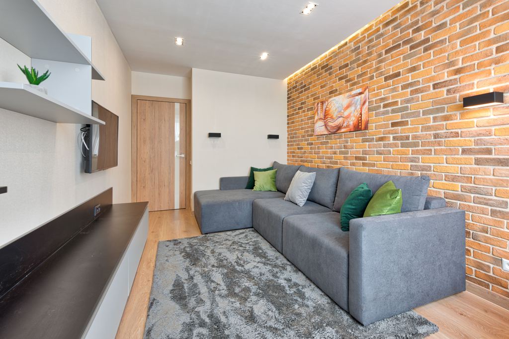 Gray L-shaped sectional sofa in a modern living room with an exposed brick wall.