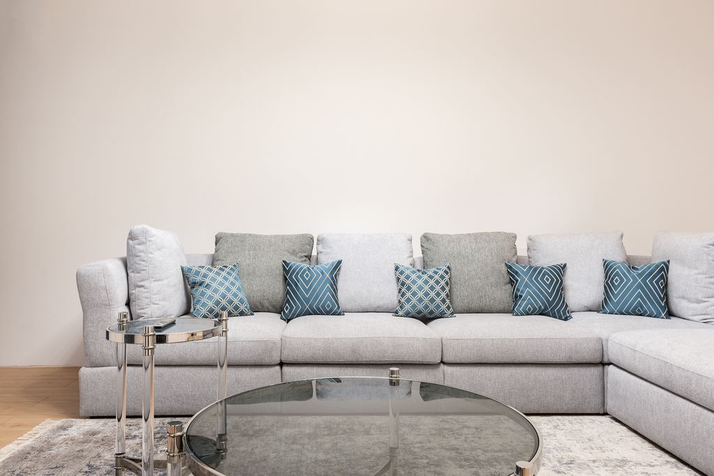 Round glass coffee table in front of a gray L-shaped sectional sofa with blue patterned pillows