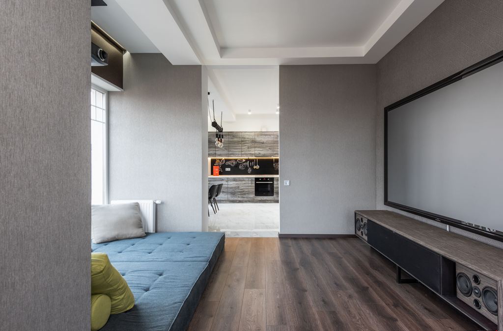 Large wall-mounted screen above a long low-profile media console with built-in speakers in a modern living room.