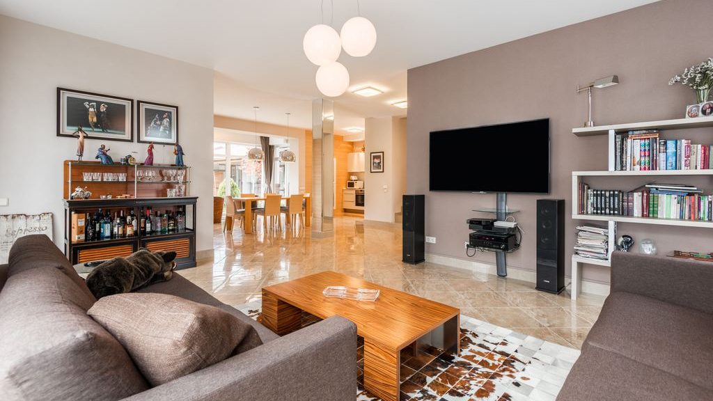Contemporary living room with gray sofas, a wall-mounted TV, open bookshelves, framed wall art, and a wood coffee table.