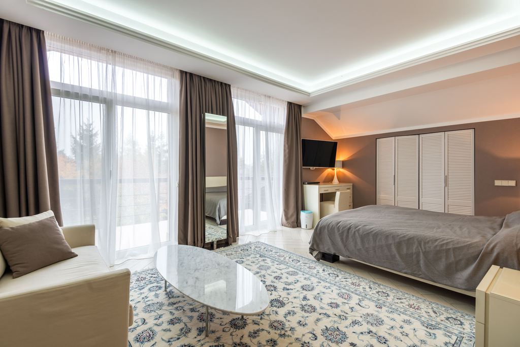 Spacious modern bedroom with a cream sofa, bed, TV, and large windows
