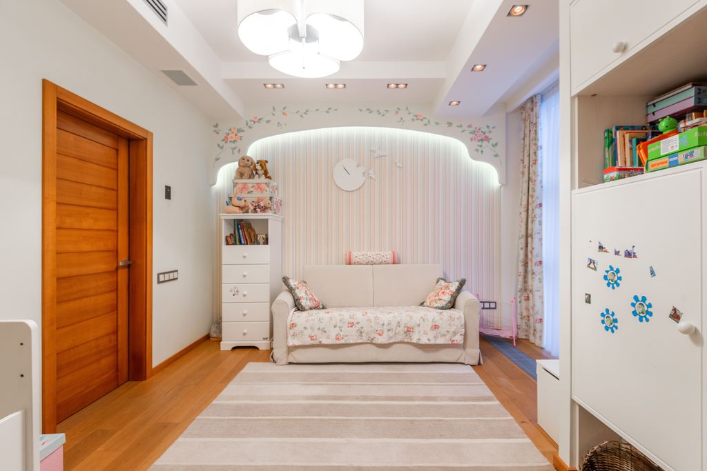 Bright kids’ room with a compact beige sofa, striped rug, bookshelves, and built-in storage.