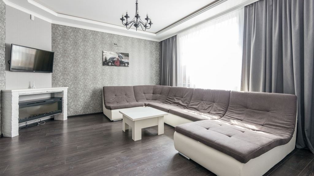 Gray sectional sofa with a chaise, white coffee table, TV, fireplace, and floor-to-ceiling curtains in a modern living room.