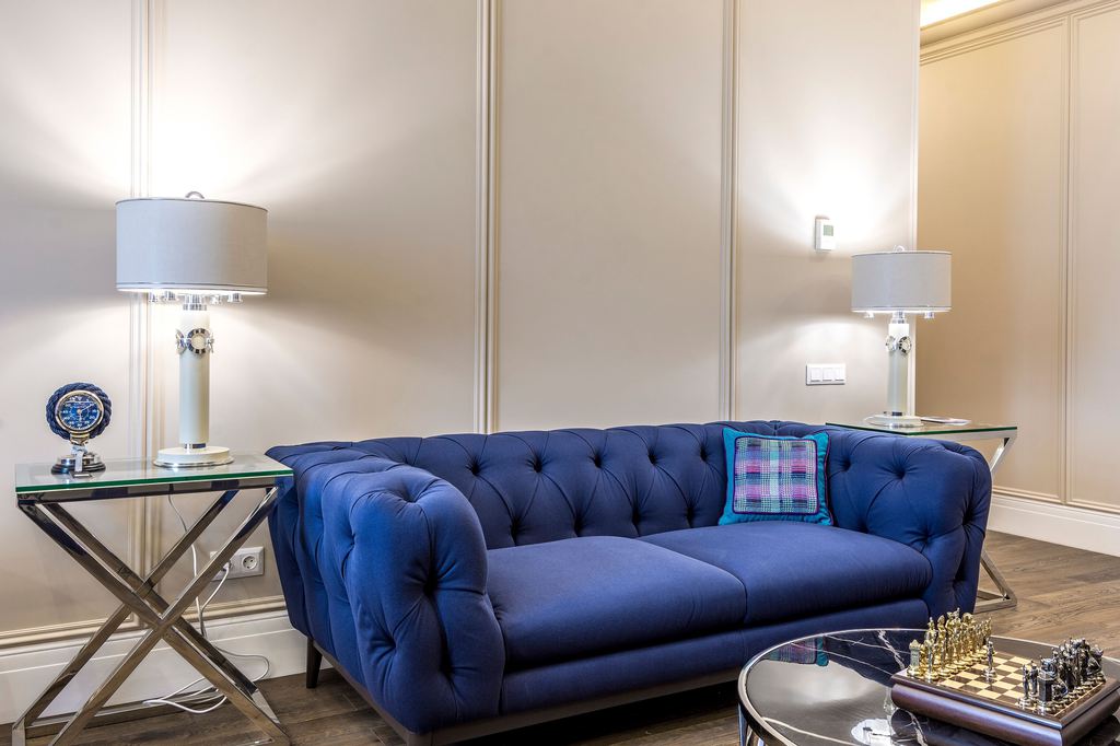 Blue tufted sofa with glass-top side tables, table lamps, and a round coffee table in an elegant living room.
