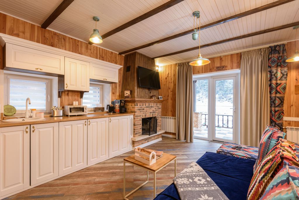 Tiny home interior with compact kitchen, wood-paneled walls, blue sofa, small coffee table, and large windows