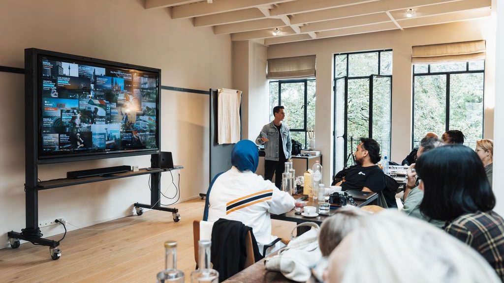 Large TV on a rolling mobile stand during a group presentation in a modern meeting room.