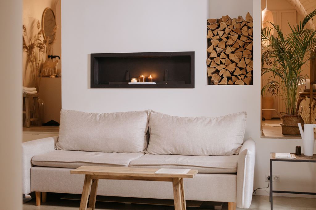 Cream sofa in a warm neutral living room with a wood bench, fireplace, and indoor plants.