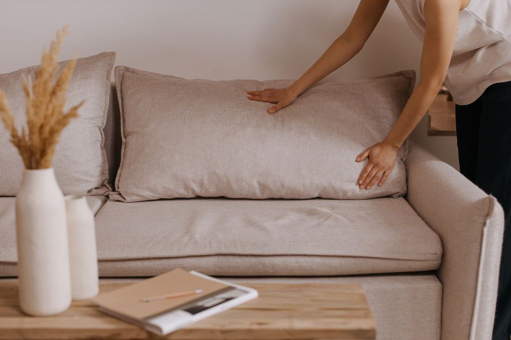 Woman checking beige sofa cushions for signs of bed bugs in a living room