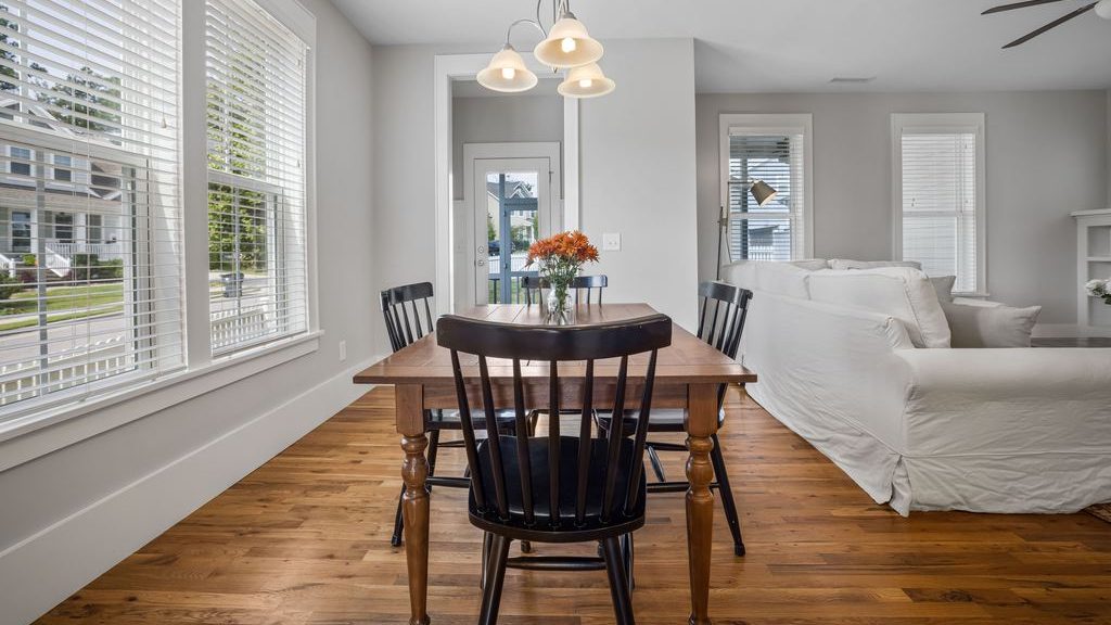Rectangular wood dining table with black chairs in a bright open-plan dining and living room.
