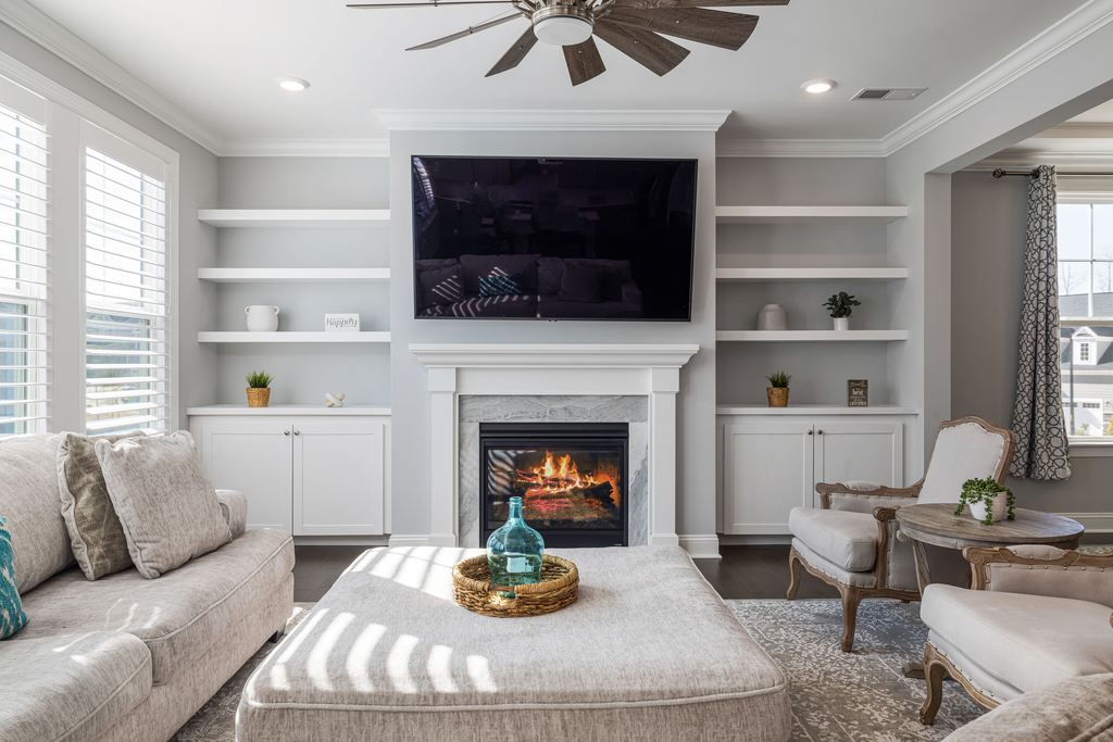 Large square upholstered ottoman used as a coffee table with a woven tray in a bright living room.