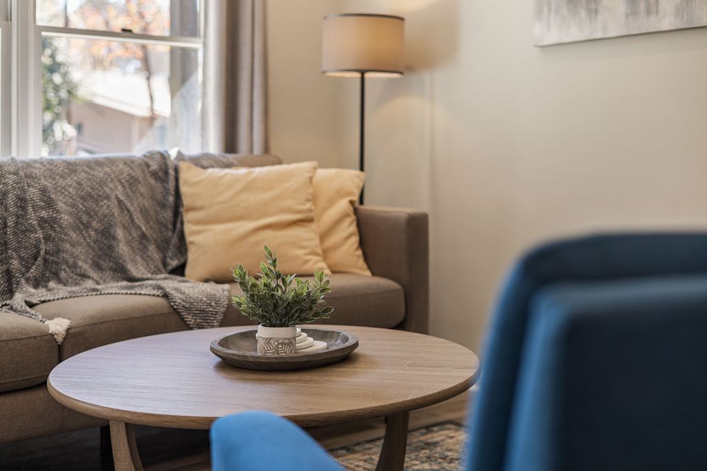 Cozy living room with a wooden round coffee table styled with a tray, small plant, and stacked books between a sofa and blue accent chairs.