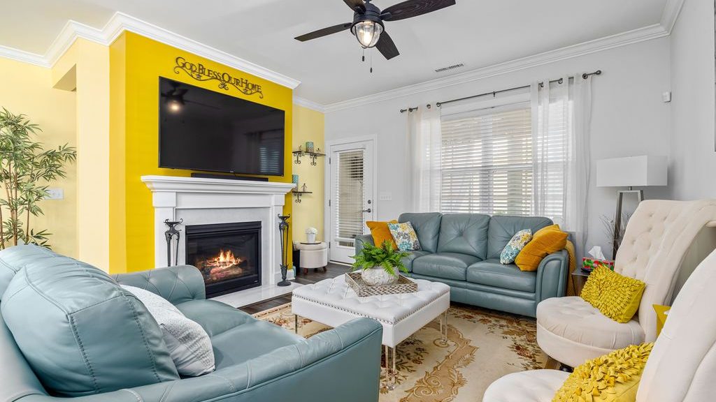 Two blue sofas and two cream accent chairs arranged around an ottoman in a conversational living room with a fireplace and wall-mounted TV.