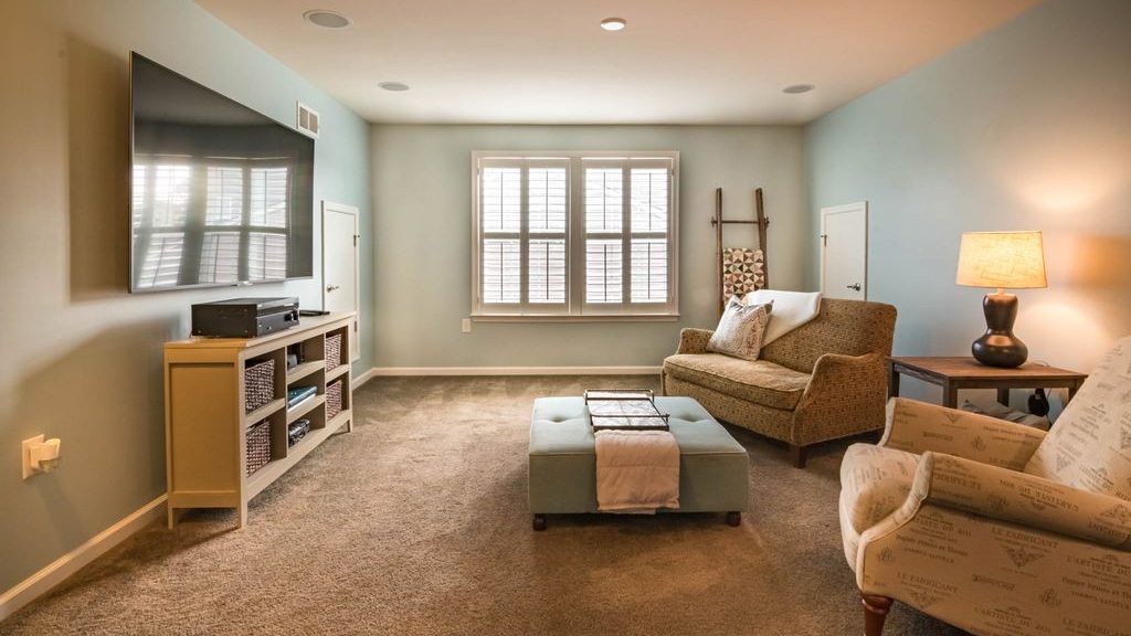 Cozy living room with a wall-mounted TV, open media console, ottoman coffee table, armchairs, and a clear viewing area.
