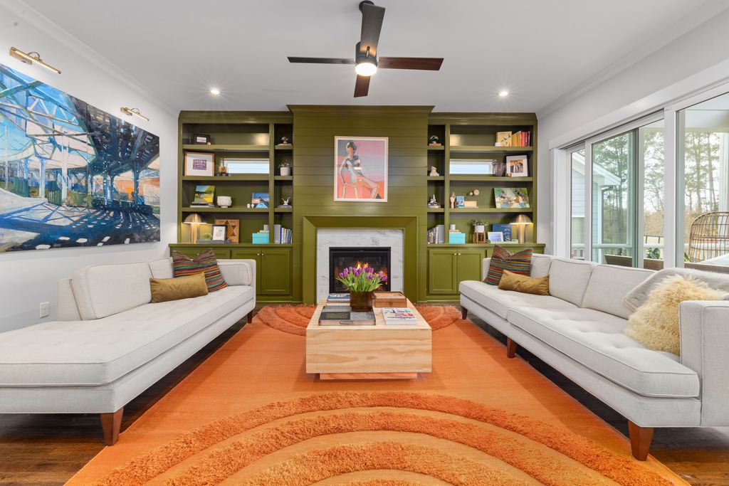 Modern living room with olive green built-in shelves, white sofas, and a large orange area rug.