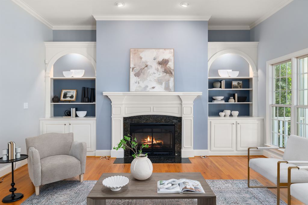 Bright living room with a white fireplace, pale blue walls, built-in shelves, neutral seating, and a simple coffee table centerpiece.