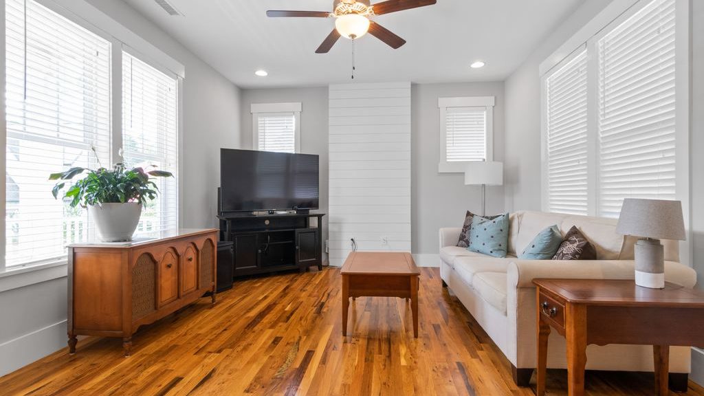 TV on a corner TV stand in a bright living room with wood furniture and white seating.