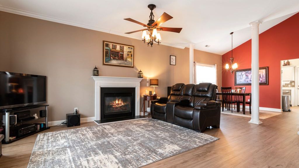 Open-concept living room with a dark leather reclining loveseat, fireplace, TV stand, large area rug, and adjacent dining area.