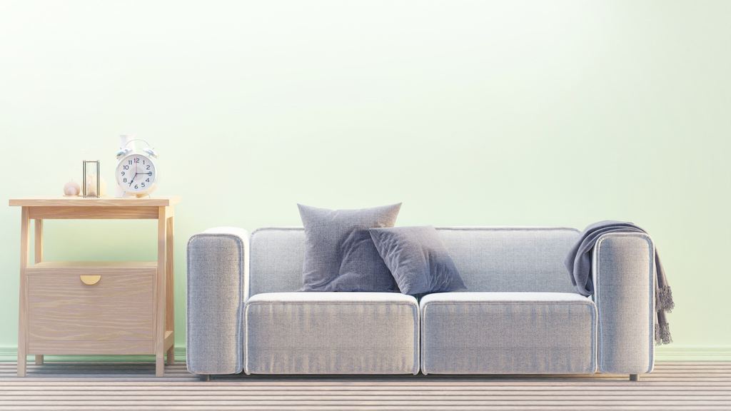 Compact gray two-seat sofa with throw pillows beside a wooden side table.