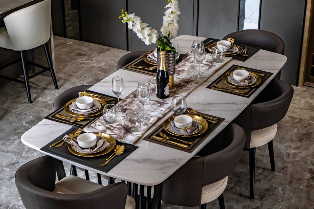Rectangular stone dining table set for six with dark upholstered chairs and black-and-gold place settings.