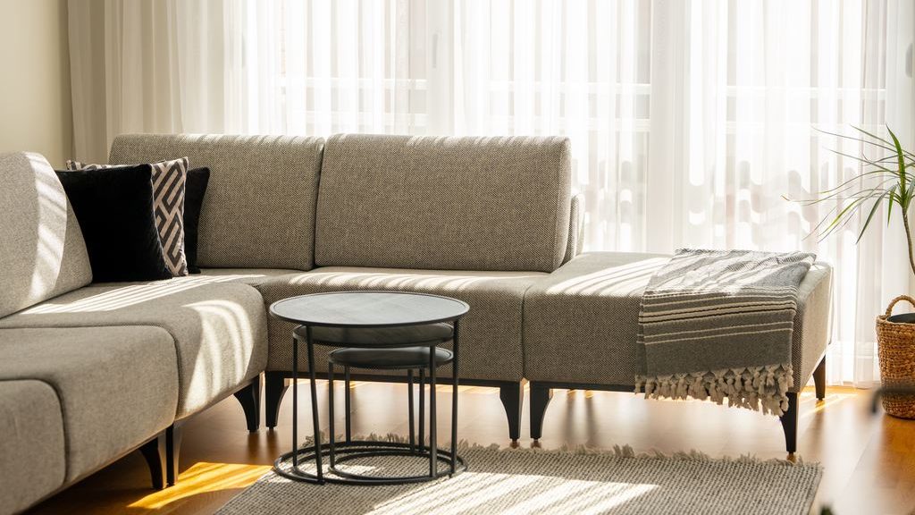 Gray sectional sofa with black nesting tables in a bright living room with sheer curtains.