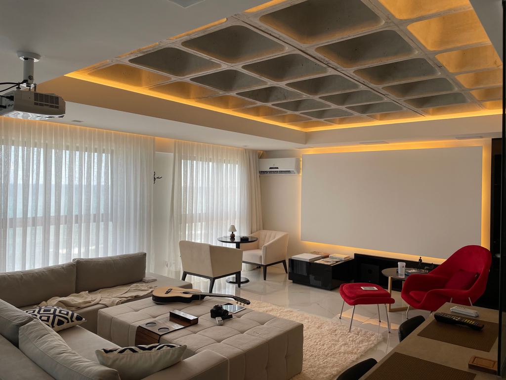 Living room home theater with a ceiling-mounted projector, large projection screen, sectional sofa, accent chairs, and warm recessed lighting.