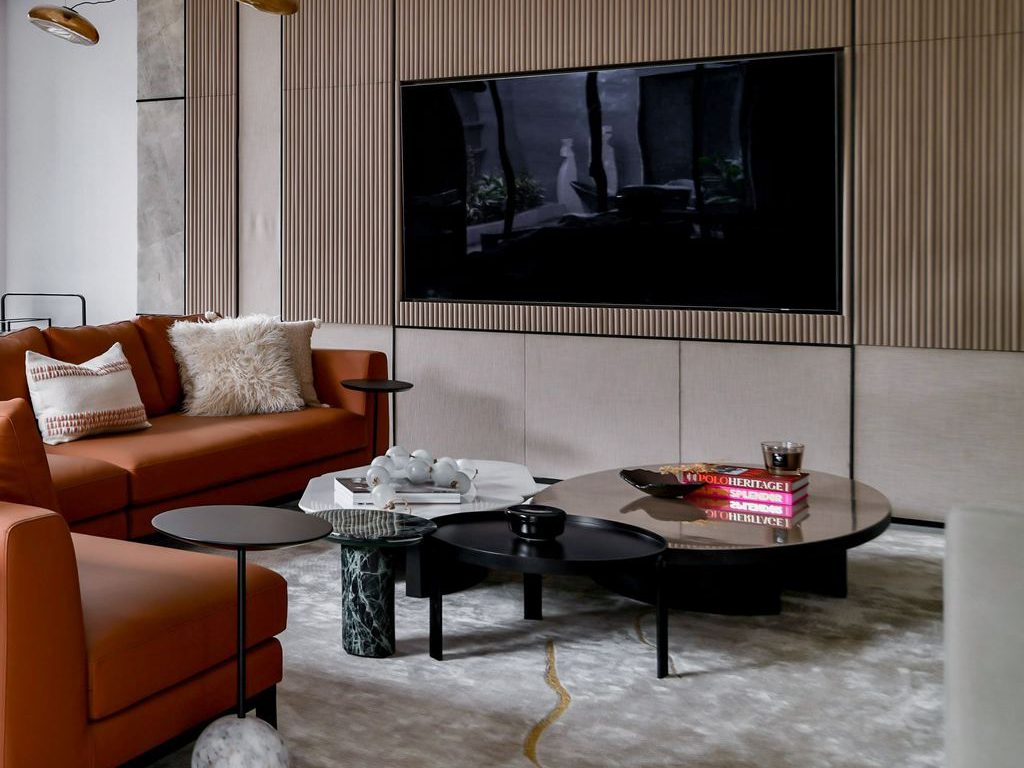 Modern living room with layered round coffee tables, leather seating, and a wall-mounted TV.