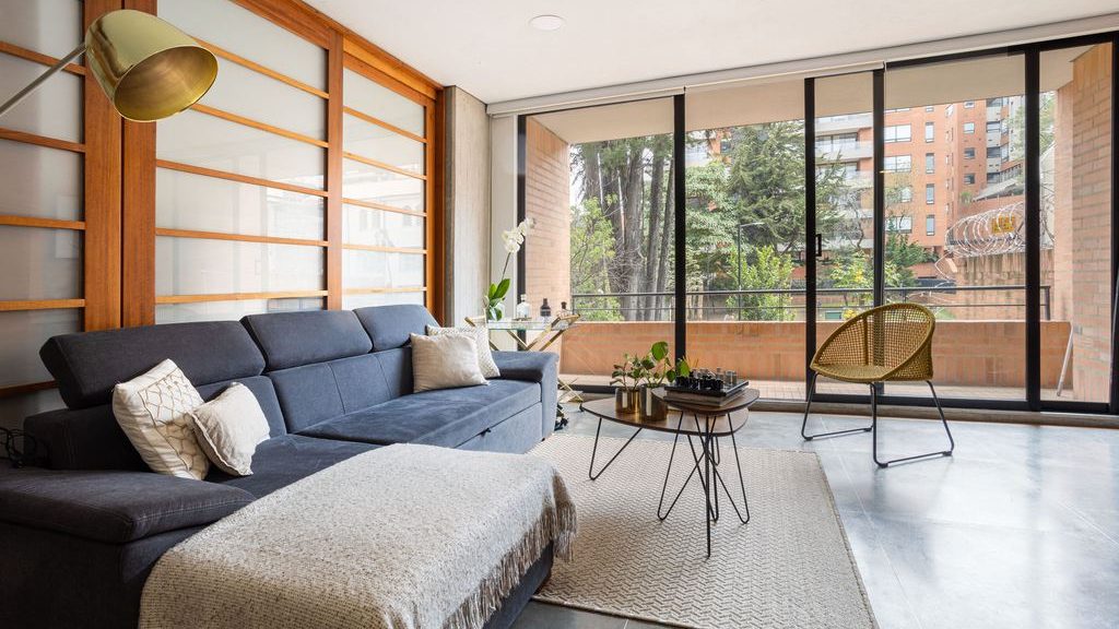 Dark blue convertible sofa bed with a chaise in a modern apartment living room with floor-to-ceiling balcony doors.