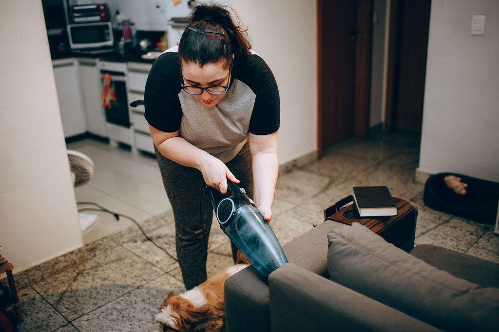 Woman vacuuming the seams of a gray sofa during bed bug cleaning and prevention