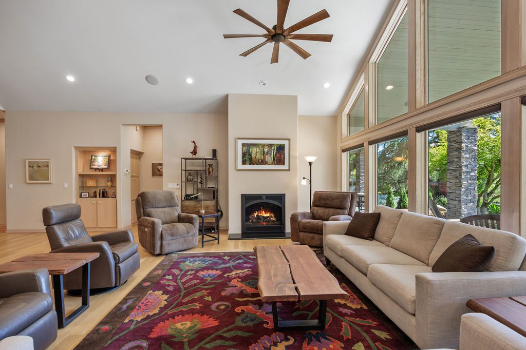 Modern living room with multiple recliners, a cream sofa, wood coffee table, colorful area rug, fireplace, and large windows.