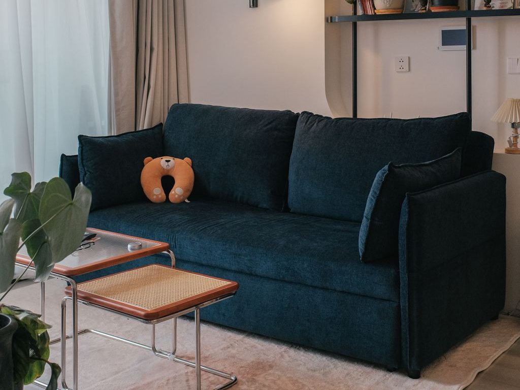 Dark blue sofa in a modern multipurpose room with a low-pile rug, side tables, shelving, and open floor space.