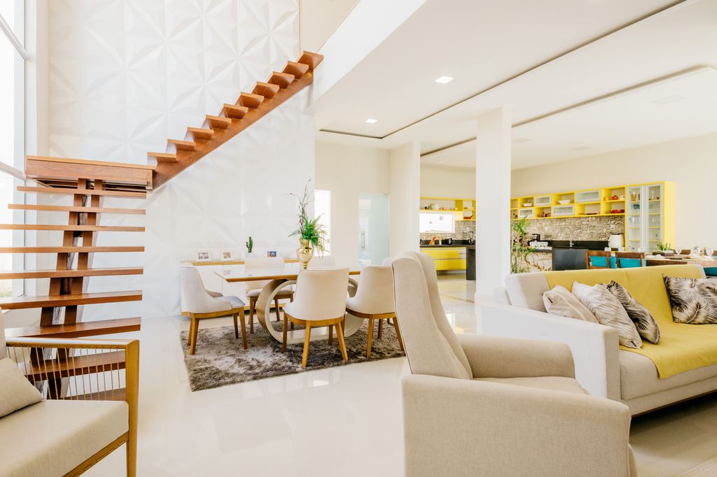 Bright open-plan living and dining room with cream seating, wood-framed chairs, a dining table, and yellow kitchen cabinetry.