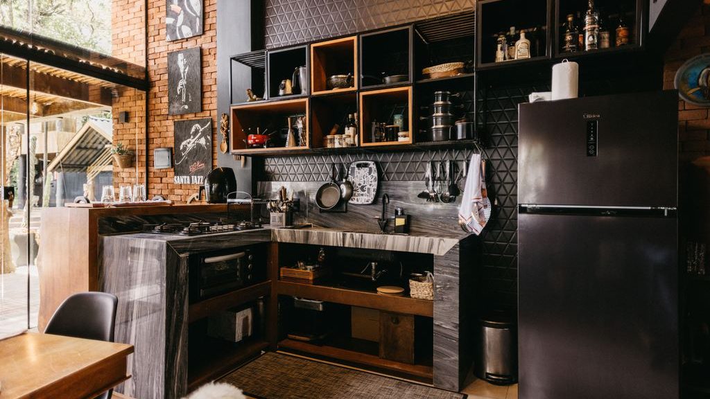 Compact tiny home kitchen with dark cabinets, open shelving, refrigerator, wood dining table, and large glass doors