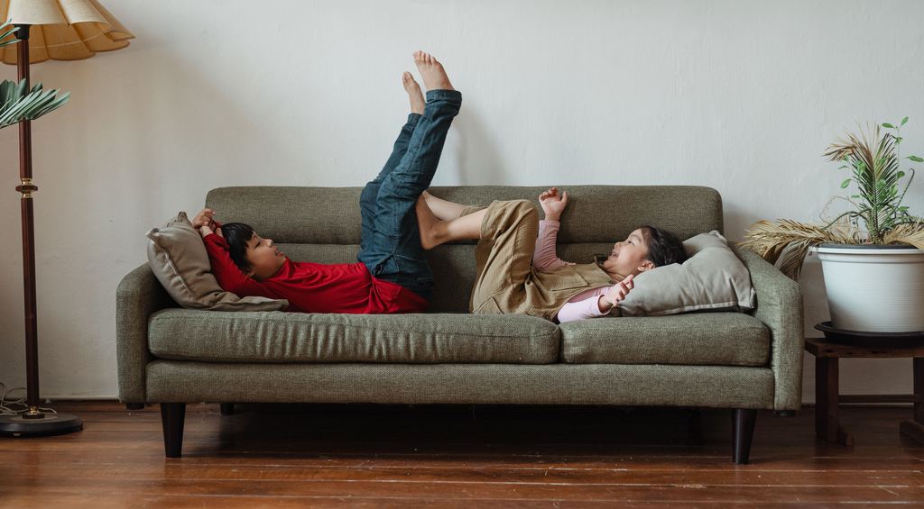 Two children playing on a gray kid-friendly sofa in a family living room