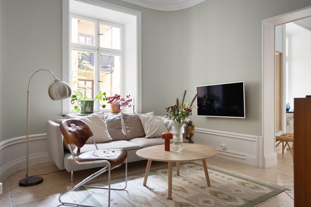 Compact light gray sofa with loose cushions in a bright Scandinavian-style living room with a wall-mounted TV.