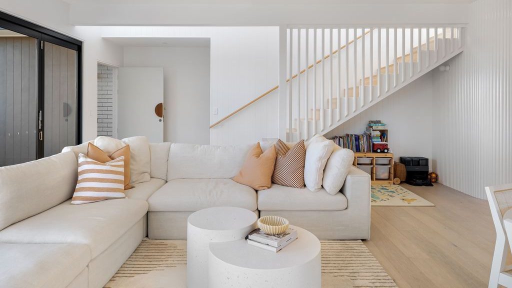 Bright family living room with a white sectional sofa, rounded nesting coffee tables, and a children’s play area under the stairs.