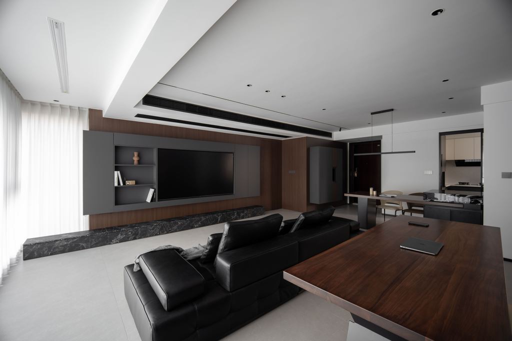 Black leather sofa in a modern open-plan living room with dark wood furniture and a wall-mounted TV.