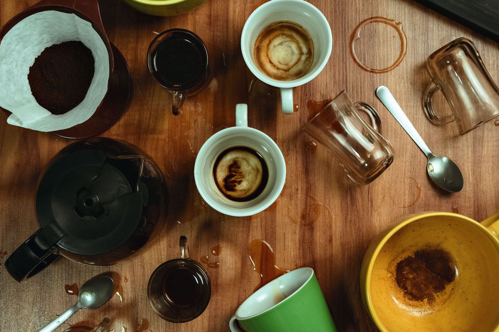 Overhead view of coffee cups, mugs, and a circular water ring on a wooden coffee table.