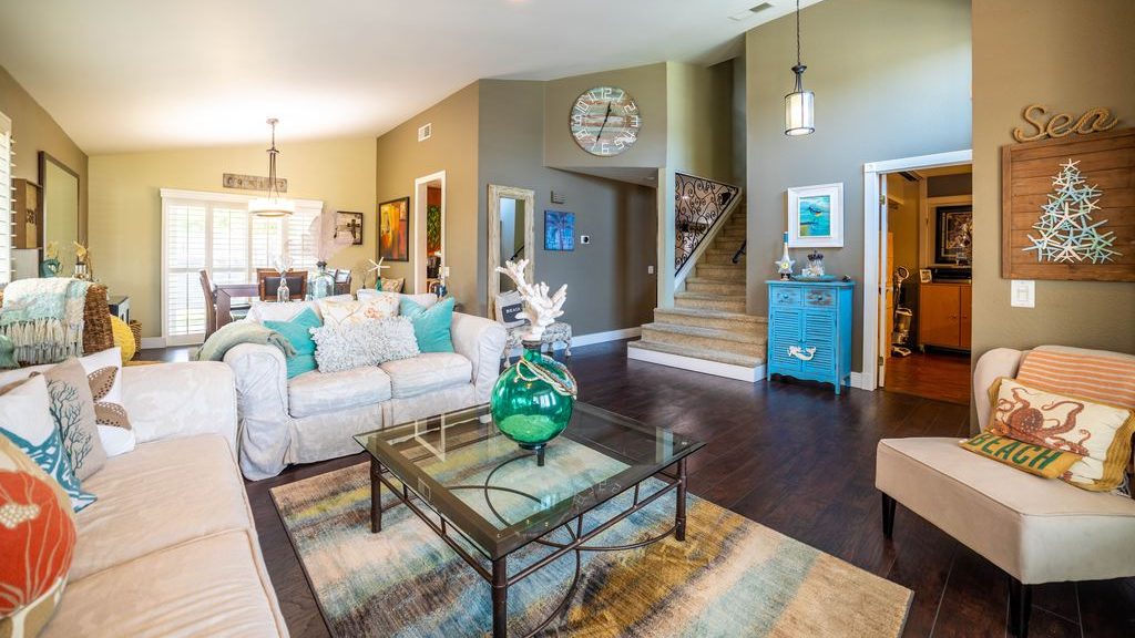 Coastal-inspired living room with white sofas, turquoise accents, a glass coffee table, and beach-themed decor.