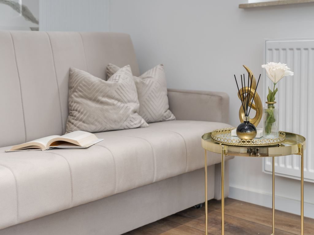 Beige sofa in a compact living room with a gold side table and decorative pillows.