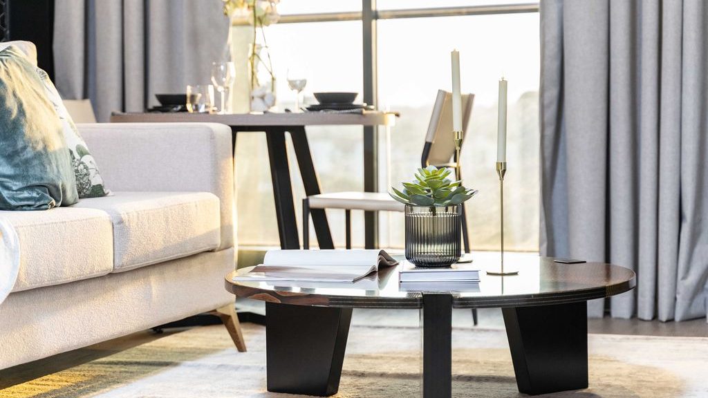 Round black coffee table styled with books, candles, and a potted plant beside a cream sofa in a modern living room.
