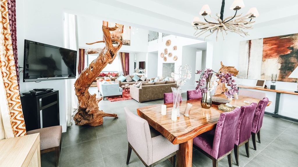 Postmodern dining and living space with a live-edge wood table, purple upholstered chairs, sculptural wood accents, and oversized abstract art.