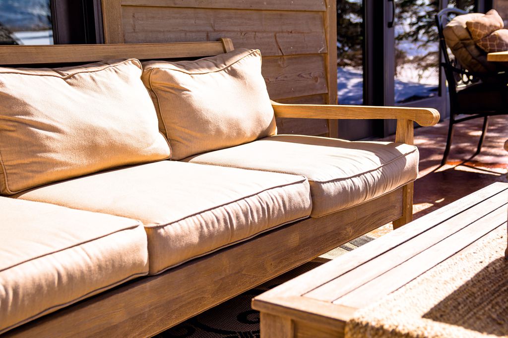 Wood-framed outdoor futon sofa with beige cushions and a matching coffee table on a sunny patio.