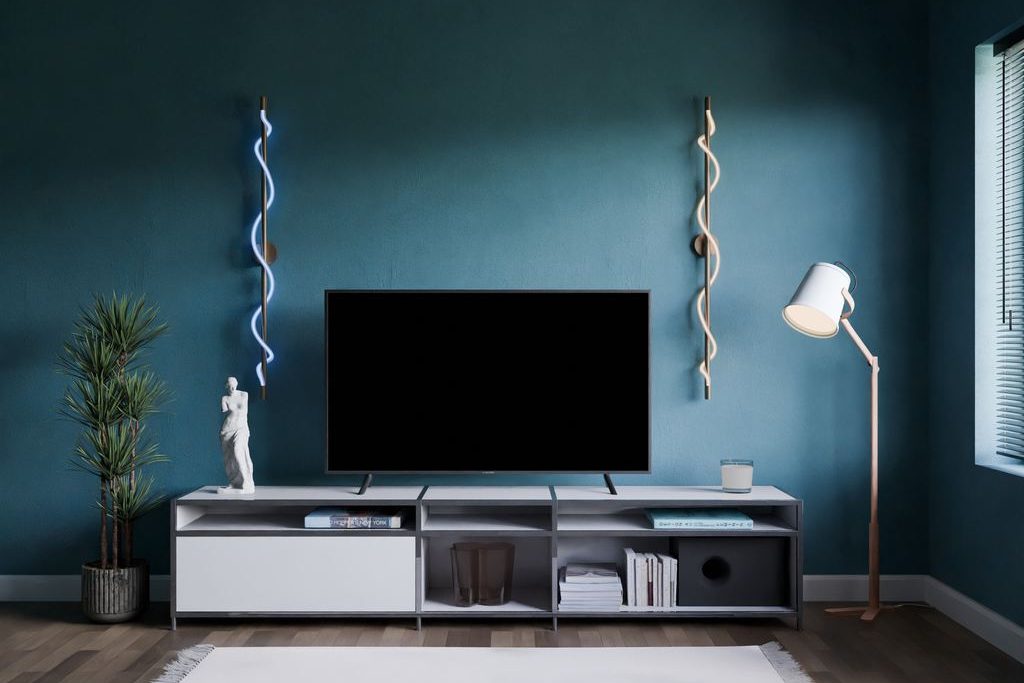 Minimalist white TV stand with open shelving against a dark teal wall, styled with a TV, books, plant, and floor lamp.