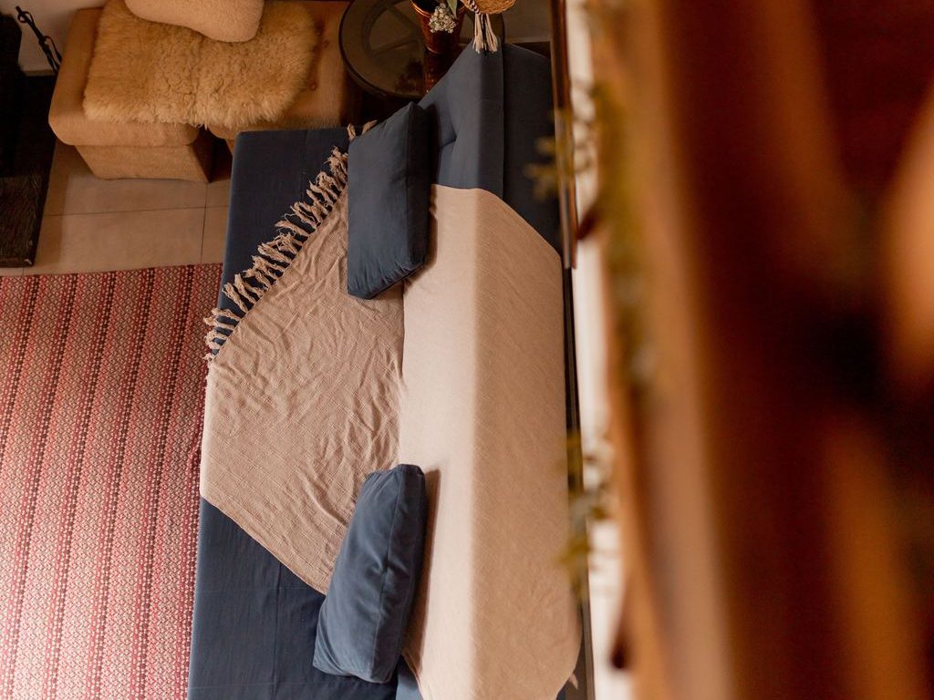 Overhead view of a blue sofa bed with pillows and a throw blanket in a warm, cozy living room.
