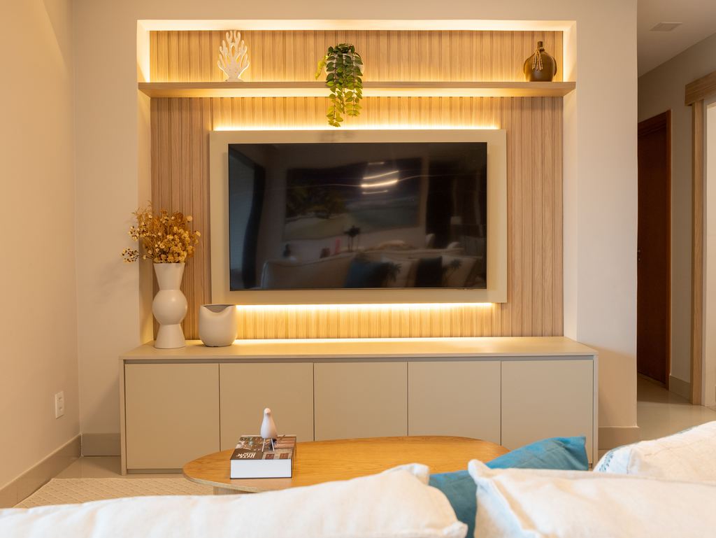 Wall-mounted TV above a low white media console with built-in lighting, wood slat paneling, and minimalist decor in a warm modern living room.