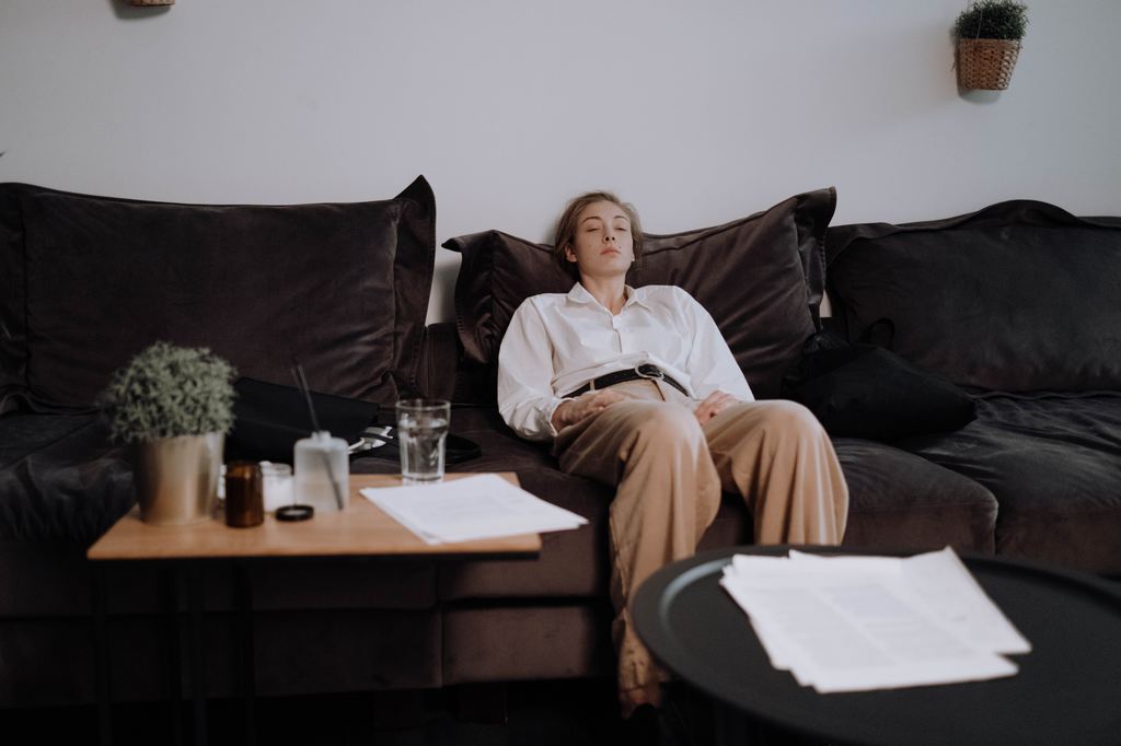 Shorter woman resting on a deep dark sofa with oversized back cushions in a living room.