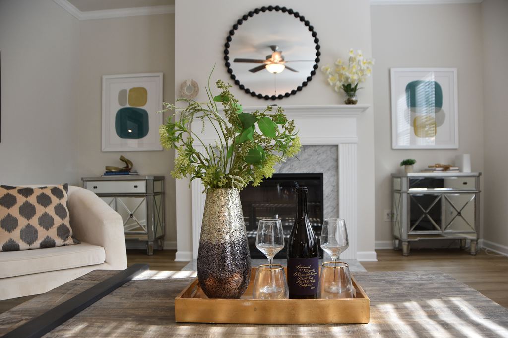 Living room coffee table with a floral vase, wine tray, mirrored consoles, and a fireplace beneath a round black beaded mirror.