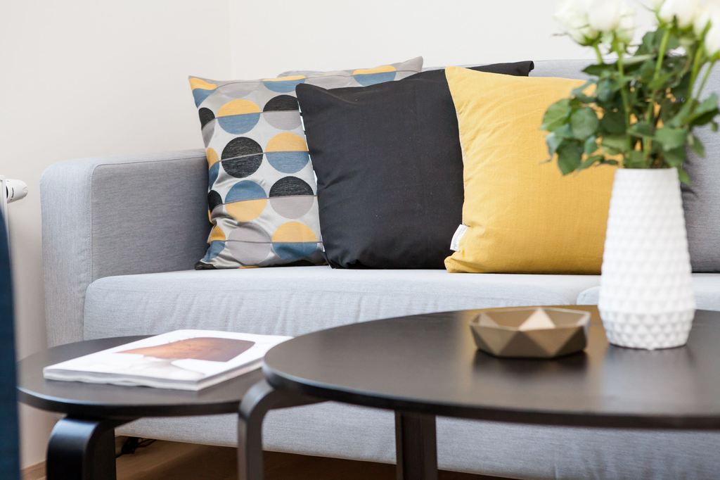 Gray sofa styled with yellow, black, and geometric throw pillows behind nesting coffee tables in a modern living room.