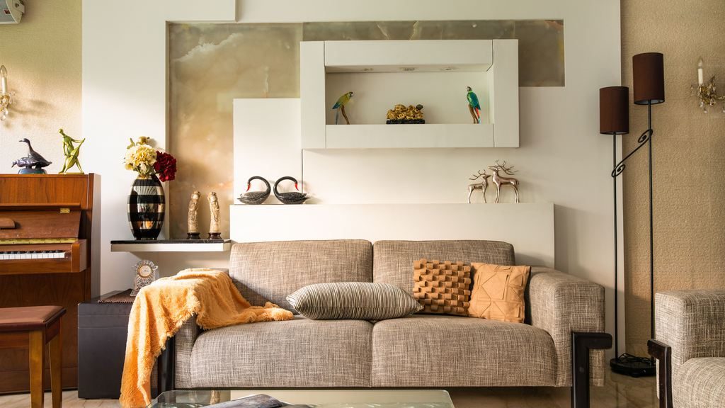 Cozy living room with a beige sofa, wall-mounted display cabinet, decorative objects, floor lamps, and warm-toned accents.