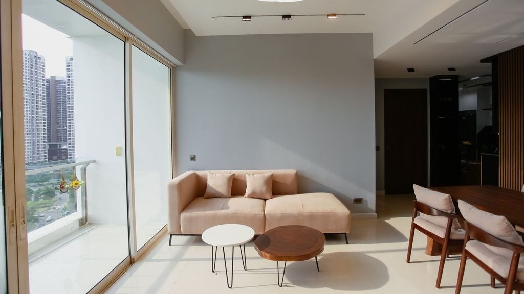Minimal tiny home living area with pink chaise sofa, nesting coffee tables, large balcony windows, dining chairs, and modern ceiling light
